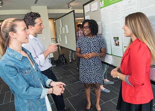 Students talking to a professor in front of a research poster