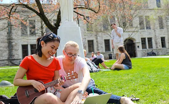 Students hanging out on the quad, one of them playing a ukelele