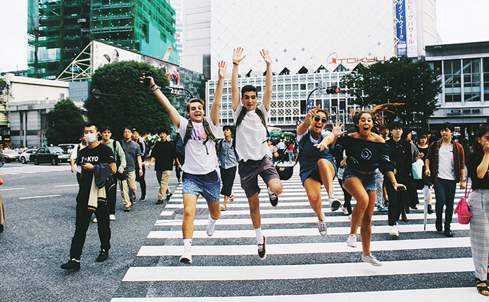 Students jumping for joy while walking through a busy crosswalk in Japan